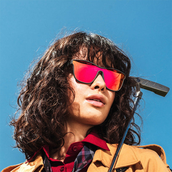 Person wearing Goodr VRG Voight Kampff Vision Sunglasses with mirrored red/orange lenses and black frame on a sky blue background.