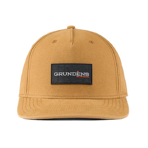 Front of the Grundens Ballast Canvas Trucker Hat in whiskey tan with a black logo patch in the center, against a white background.