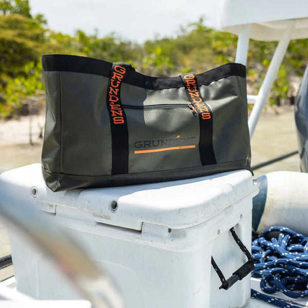 An anchor grey Grundéns Gear Hauler 50L Tote Bag on a boat deck, with mangroves in the background.