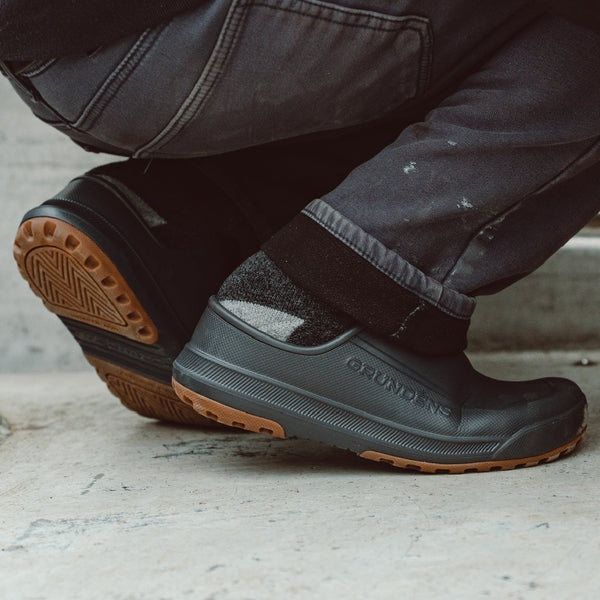 Person wearing jeans and a pair of anchor grey Grundens Men's Fish-On Slip-On shoes on pavement.