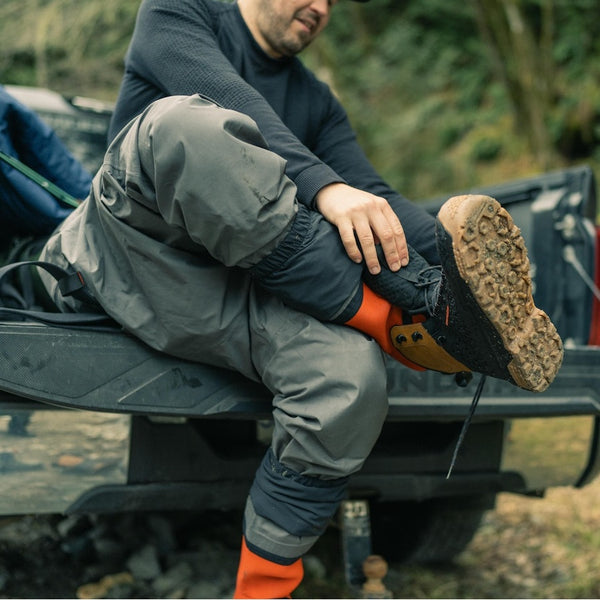 Person changing our of waders and the on Grundens Men's Rock Armor Wading Boots while sitting on a truck tailgate.