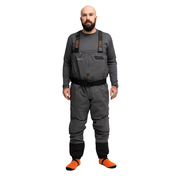 Person wearing the Grundéns Men's Vector Stockingfoot Wader featuring anchor grey material with black belt and gravel guards and orange neoprene booties, against a white background.
