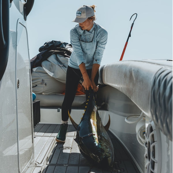 Person holding a large fish on a tuna boat and wearing the Light zephyr blue Grundens Women's Tough Sun UPF Hoody.