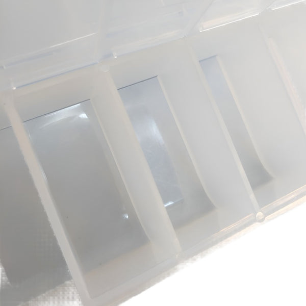 Close up of the beveled compartments clear acrylic Hareline Hook Box Pro with multiple compartments, designed for storing fly tying hooks and beads, against a white background.