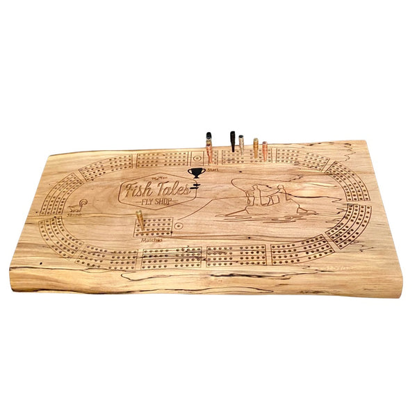 Angled view of a 4-track wooden cribbage board made with live edge black walnut with engraved fly fishing design, on a white background.