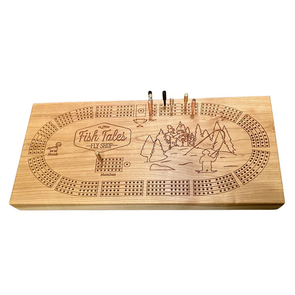 Angled view of a 4-track wooden cribbage board made with cherry wood with engraved fly fishing design, on a white background.
