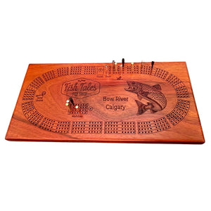 Angled view of a 4-track wooden cribbage board made with sapele with engraved fly fishing design, on a white background.