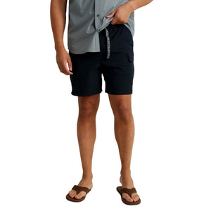 front view of a man wearing black huk fishing men's creekbed cargo shorts and leather flip flops on a white background