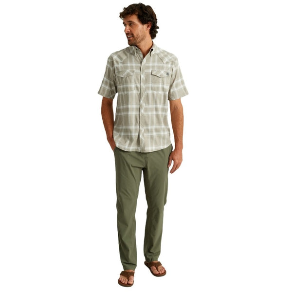view of a man wearing moss green huk fishing men's creekbed wet wading pants and a sort sleeved shirt on a white background