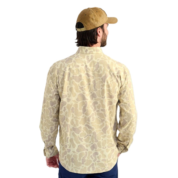 Man wearing a Huk KC Sand Camo Long-Sleeve Tide Point Shirt and brown cap on a white background.