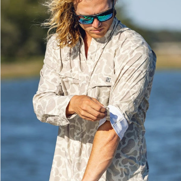 Man wearing a Huk KC Sand Camo Long-Sleeve Tide Point Shirt on a blurred background.