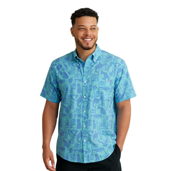 front view of a man wearing a tiki beach print marine blue color huk fishing men's kona button down short sleeve shirt on a white background