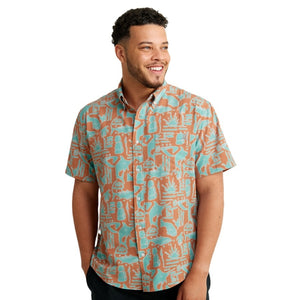 front view of a man wearing a tiki beach print sunburn color huk fishing men's kona button down short sleeve shirt on a white background