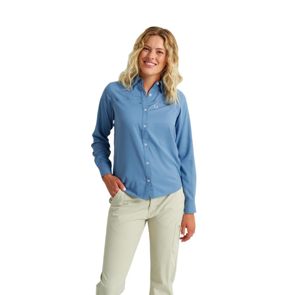 front view of a woman wearing a light blue huk fishing womens tide point button down long sleeve shirt and khaki pants on a white background