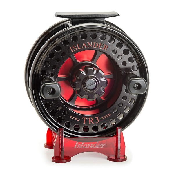 The Islander TR3 Trolling Reel - Oyster River Edition in black with red engraved artwork showing spool handles on a stand, against a white background.