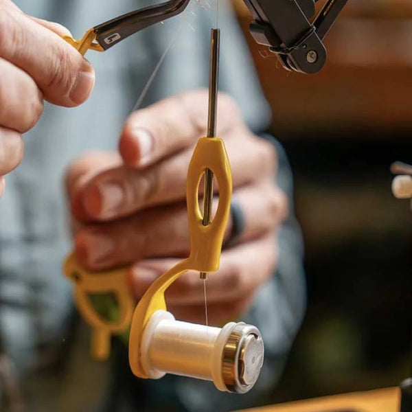 Person using a Loon Outdoors Ergo Dialed-In Fly Tying Bobbin on a fly tying vised with white thread, on a white background.