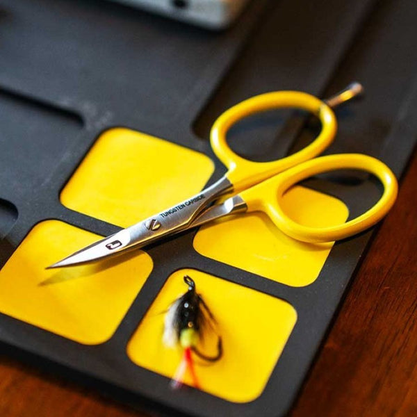 A set of Loon Outdoors Tungsten Carbide Curved Fly Tying Scissors with a yellow powder coated handle, precision peg, and Tungsten Carbide cutting blades, on Loon fly tying mat with a fly.