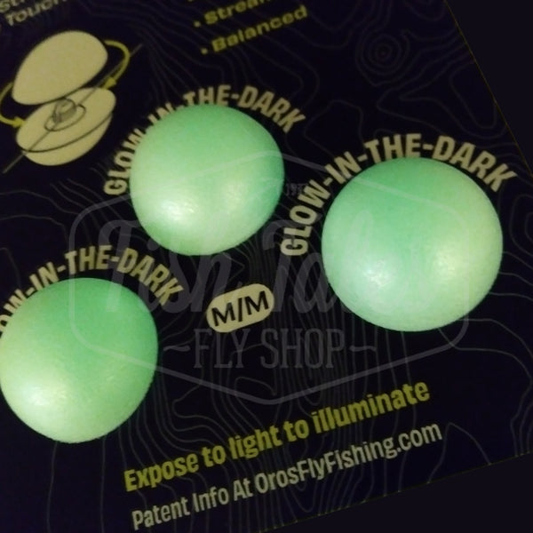 Packaged OROS strike indicators with three glow-in-the-dark medium sized indicators included and glowing, on a black background.