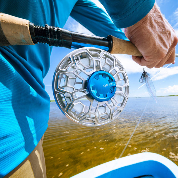 Close-up of an Orvis Ratio fly fishing reel on a rod with a blurred background of water and sky.