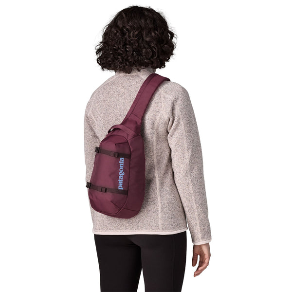 Person wearing neutral clothing and a berry fig Patagonia Atom Sling Pack on a white background.