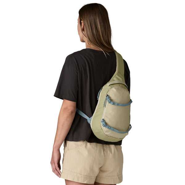 Person wearing neutral clothing and a weathered stone Patagonia Atom Sling Pack on a white background.