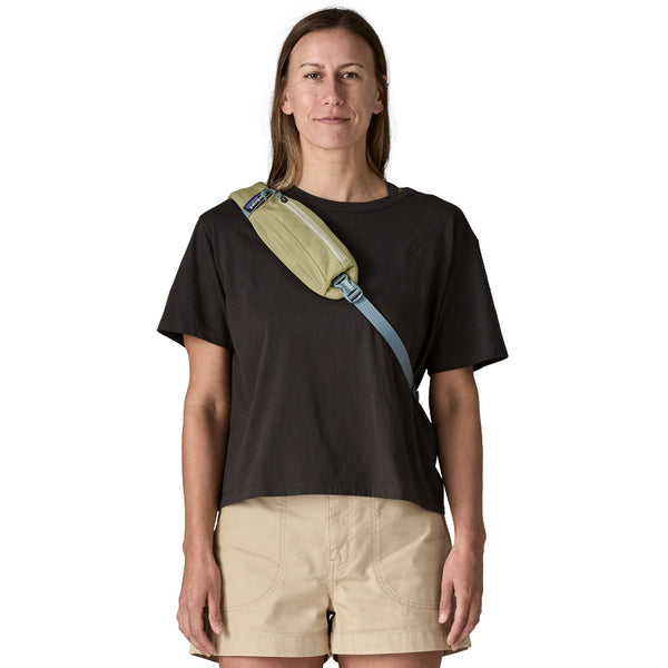 Person wearing neutral clothing and a weathered stone Patagonia Atom Sling Pack on a white background.