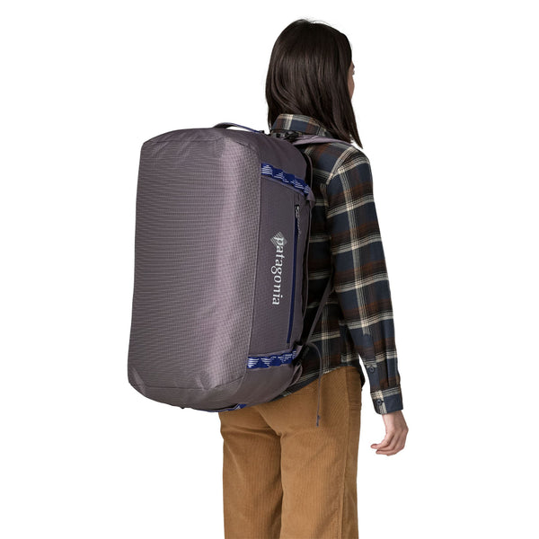 Person wearing the backpack version of the Hut Tripper: May Grey 55-Liter Patagonia Black Hole Duffel Bag showing side logo and pocket with blue accents, on a white background.