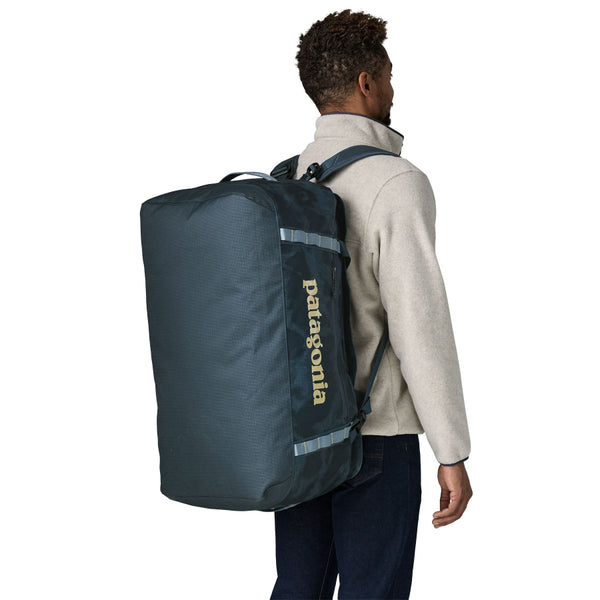 Person wearing as a backpack the sastrugi summit blue 70-Liter Patagonia Black Hole Duffel Bag showing side logo and pocket, on a white background.