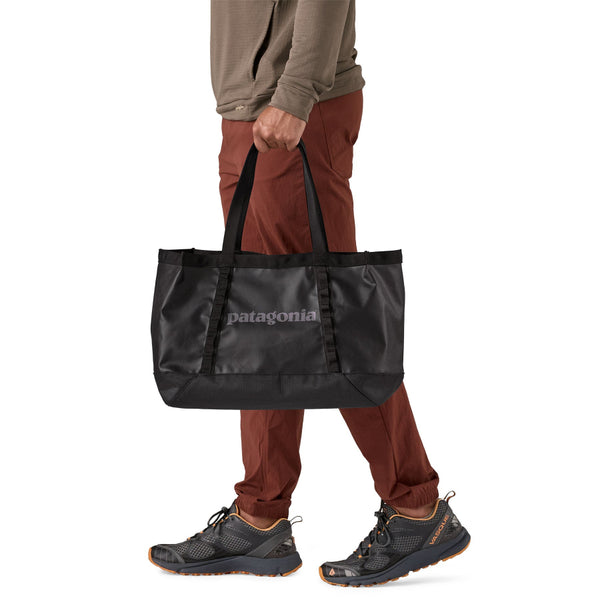 Person wearing red pants and holding the 25-liter Patagonia Black Hole Gear Tote in black with black on a white background.