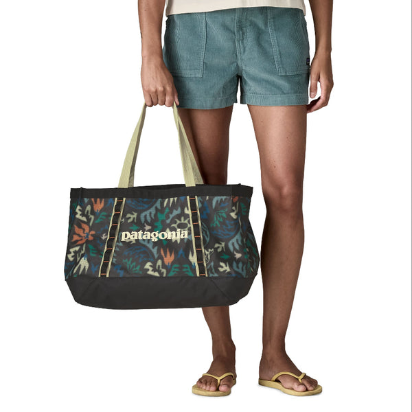 Person wearing shorts and holding the 25-liter Patagonia Black Hole Gear Tote in kaleido black on a white background.