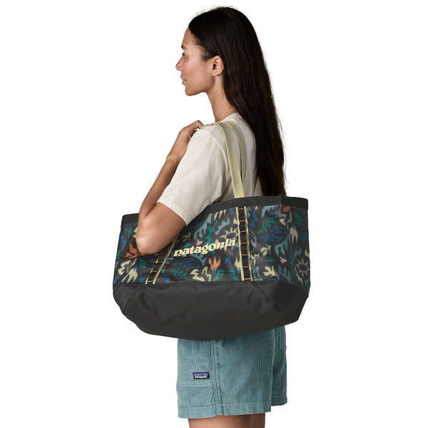 Person wearing shorts and t-shirt and and carrying the 25-liter Patagonia Black Hole Gear Tote in kaleido black on a white background.