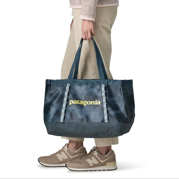 A person in tan pants carrying the 25-liter Patagonia Black Hole Gear Tote in sastrugi: summit blue color on a white background.