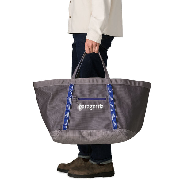 Person wearing black pants and holding the 61-liter Patagonia Black Hole Gear Tote in hut tripper: May grey color on a white background.
