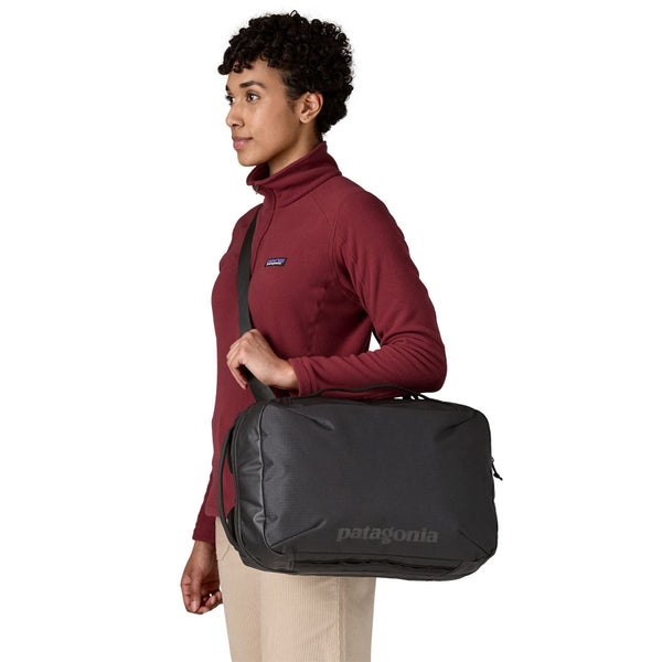 A person wearing a Black Patagonia Black Hole Micro MLC backpack with the side strap on a white background.
