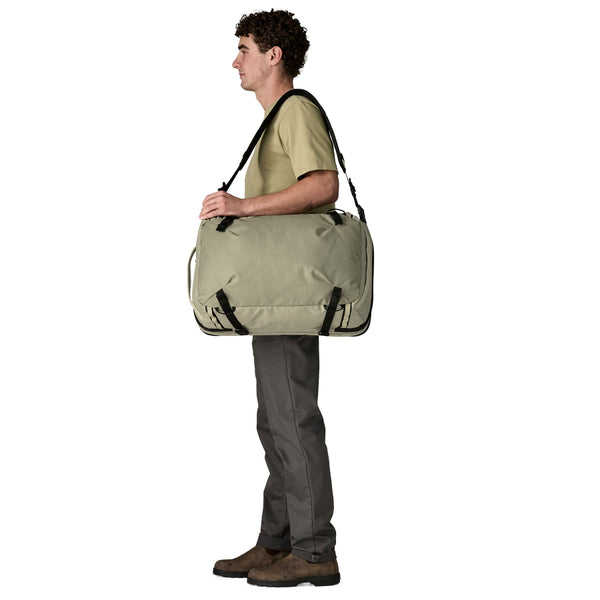Person carrying a weathered stone Patagonia Black Hole MLC Briefcase Backpack 45L over the shoulder, on a white background.