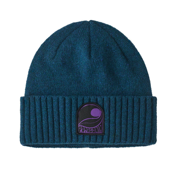 A dark teal knit Patagonia Brodeo Beanie Hat with a folded cuff, featuring a black and purple embroidered patch on the front, against a white background.