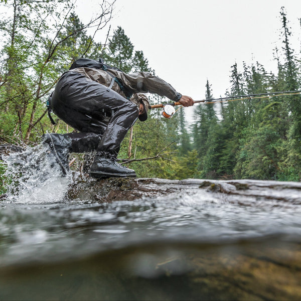 Person fly fishing in a forest stream wearing Patagonia waders and boots.