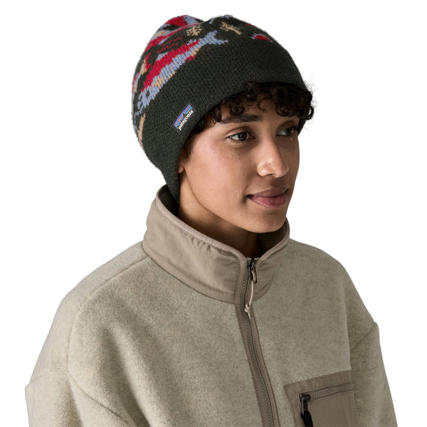 Person wearing a grey Patagonia Fun Hog Knit beanie with colorful salmon designs, and a light tan jacket over a white background.