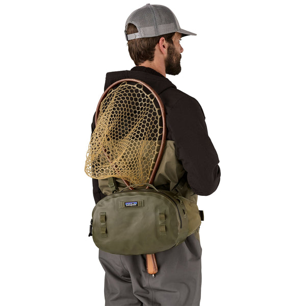 Man wearing a basin green Patagonia Guidewater Hip Pack with a fishing net on a white background.