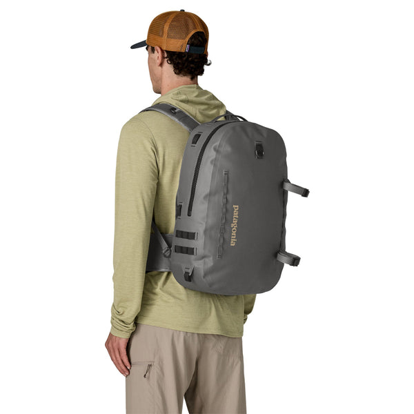 A person shown from the back wearing a light green sun hoody and the forge grey 25-Liter Patagonia Guidewater Waterproof Backpack on a white background.