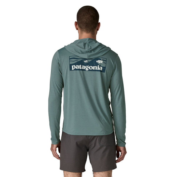 Person wearing black shorts the blue sage color Patagonia Men's Capilene Cool Daily Hoody with large Boardshort Logo on the back, against a white background.