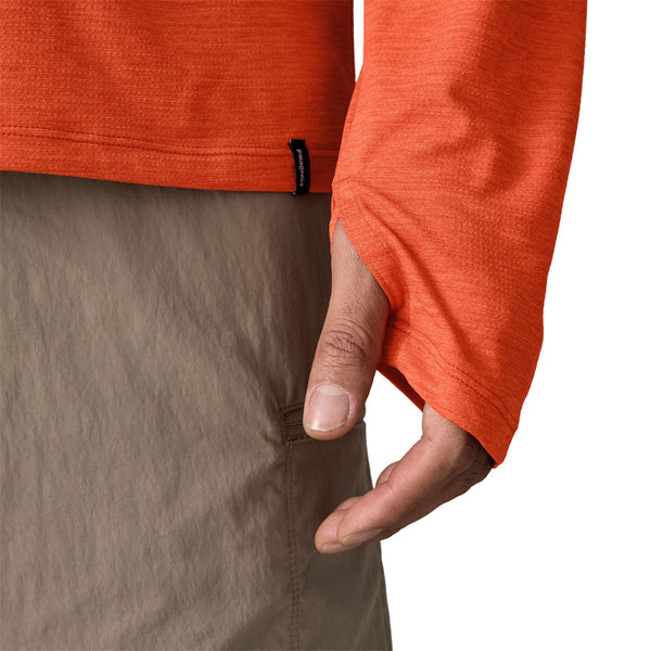 Person wearing a coal orange x-dye Patagonia Men's Capilene Cool Sun Hoody showing sleeve thumb loop details, against a white background.