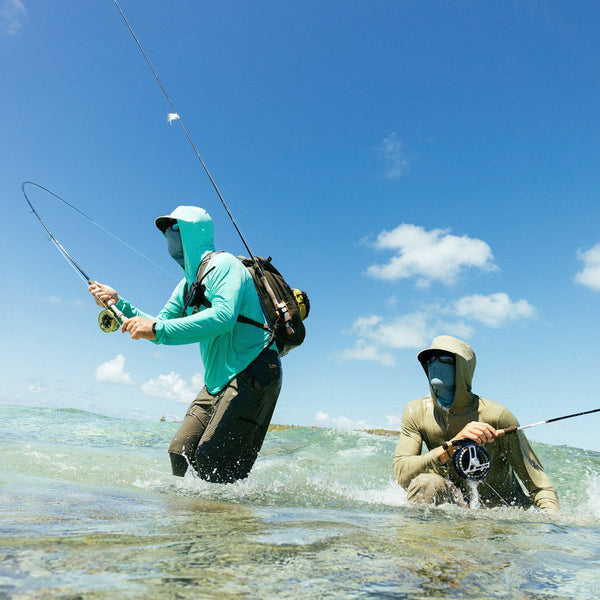 Two people fly fishing on saltwater flats, one in a light blue Patagonia Capilene Cool Sun Hoody casting a fly rod, and the other kneeling and watching in a green Patagonia Capilene Cool Sun Hoody.