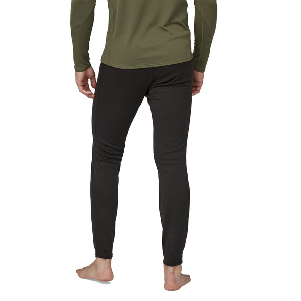 Person wearing a green long-sleeve shirt and black Patagonia Men's Capilene Midweight Bottoms on a white background.