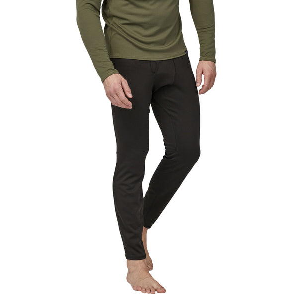 Person wearing a green long-sleeve shirt and black Patagonia Men's Capilene Midweight Bottoms on a white background.