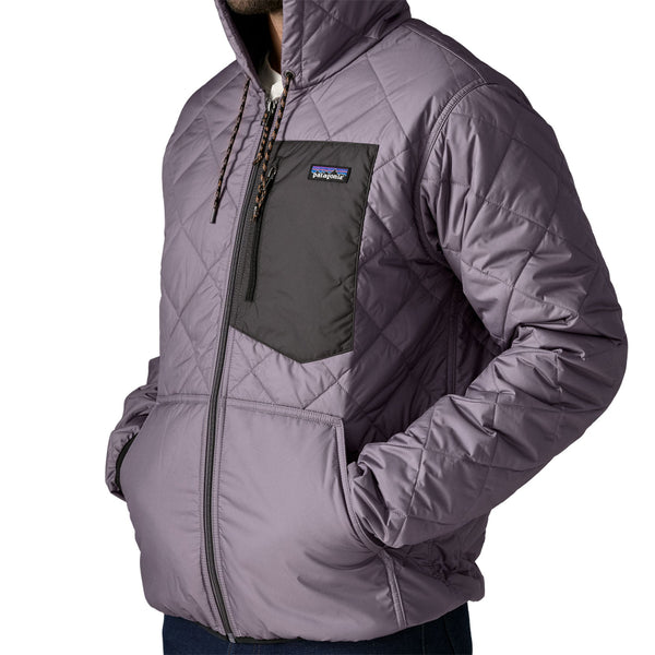 Person wearing the May Grey Patagonia Men's Diamond Quilted Bomber Hoody and jeans, showing the front hand pockets in use, on a white background.