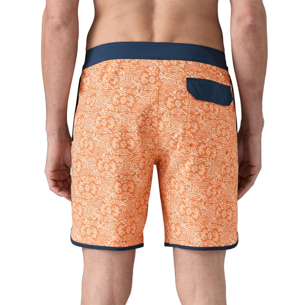 Person wearing Patagonia men's hydropeak side shore board shorts with an orange pattern and grey waistband on a white background.