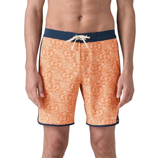 Person wearing Patagonia men's hydropeak side shore board shorts with an orange pattern and grey waistband on a white background.