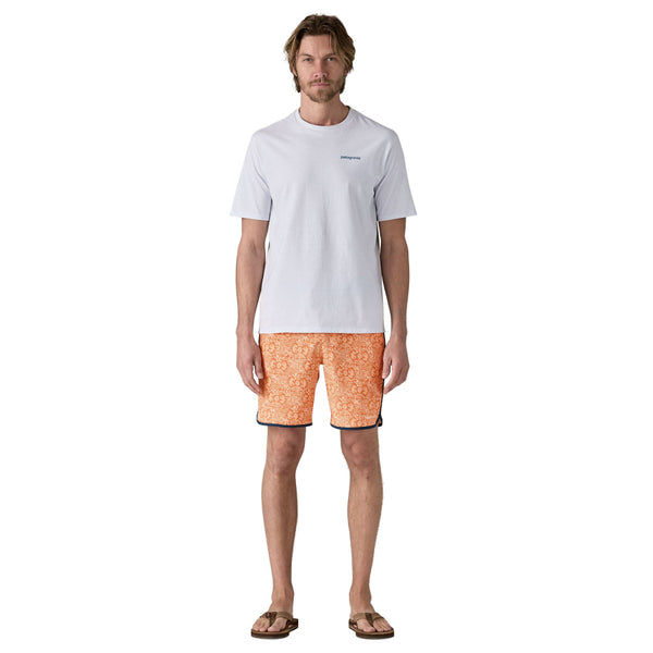 Person wearing a white tee and Patagonia men's hydropeak side shore board shorts with an orange pattern and grey waistband on a white background.