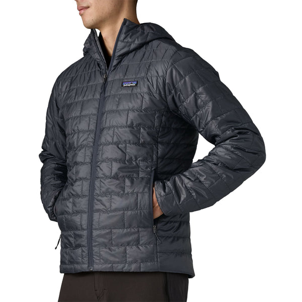 Person wearing black pants and a smolder blue Patagonia Men's Nano Puff Insulated Hoody, showing the side zipper pocket details, against a white background.